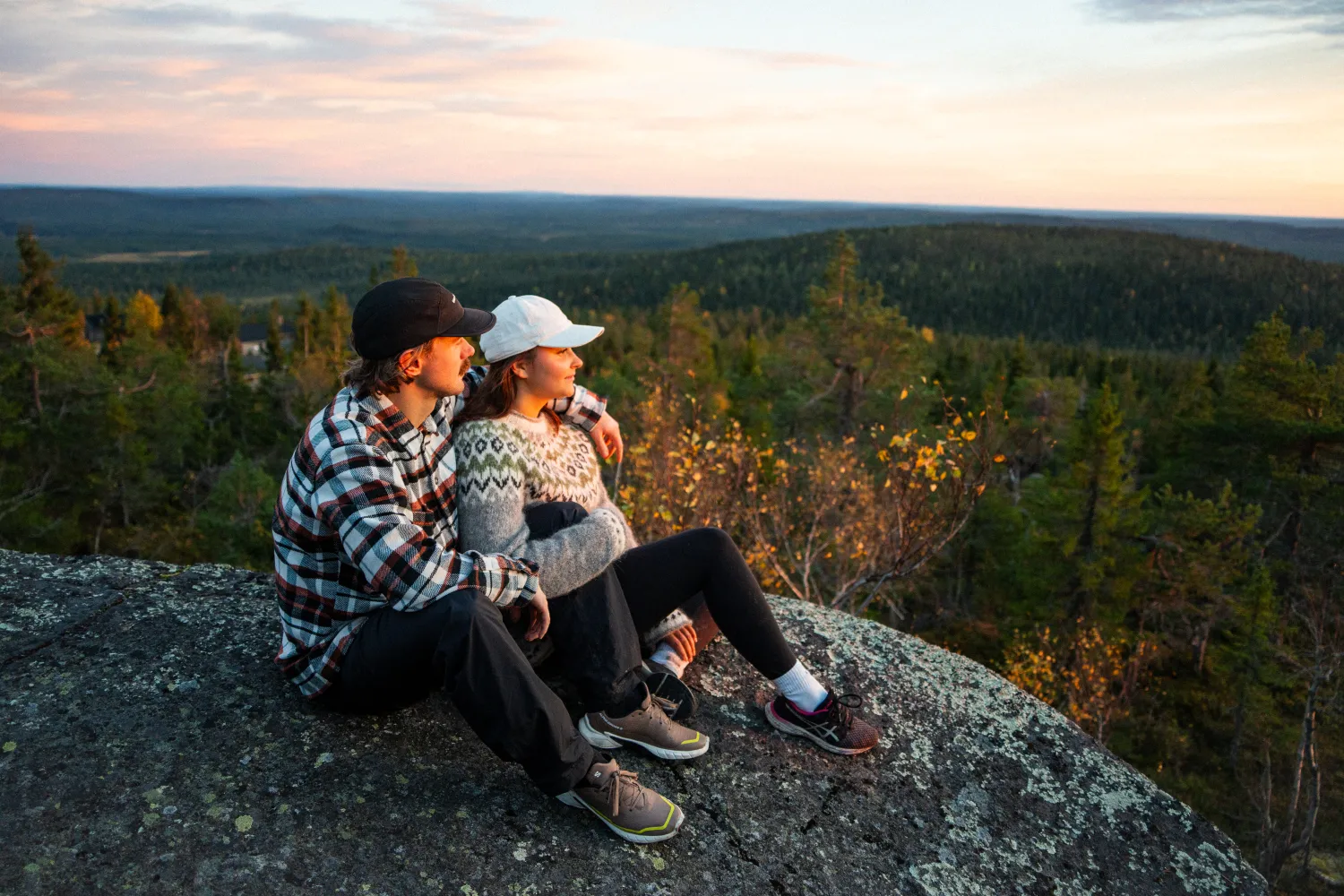 tunturin huipulla kaksi ihmistä istuu ruskan aikaan sylikkäin