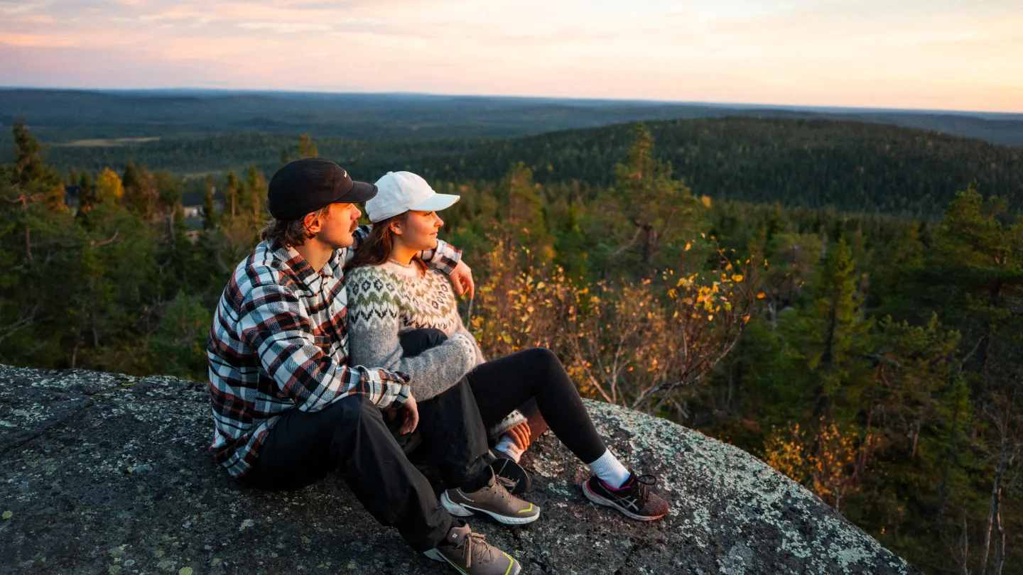 tunturin huipulla kaksi ihmistä istuu ruskan aikaan sylikkäin